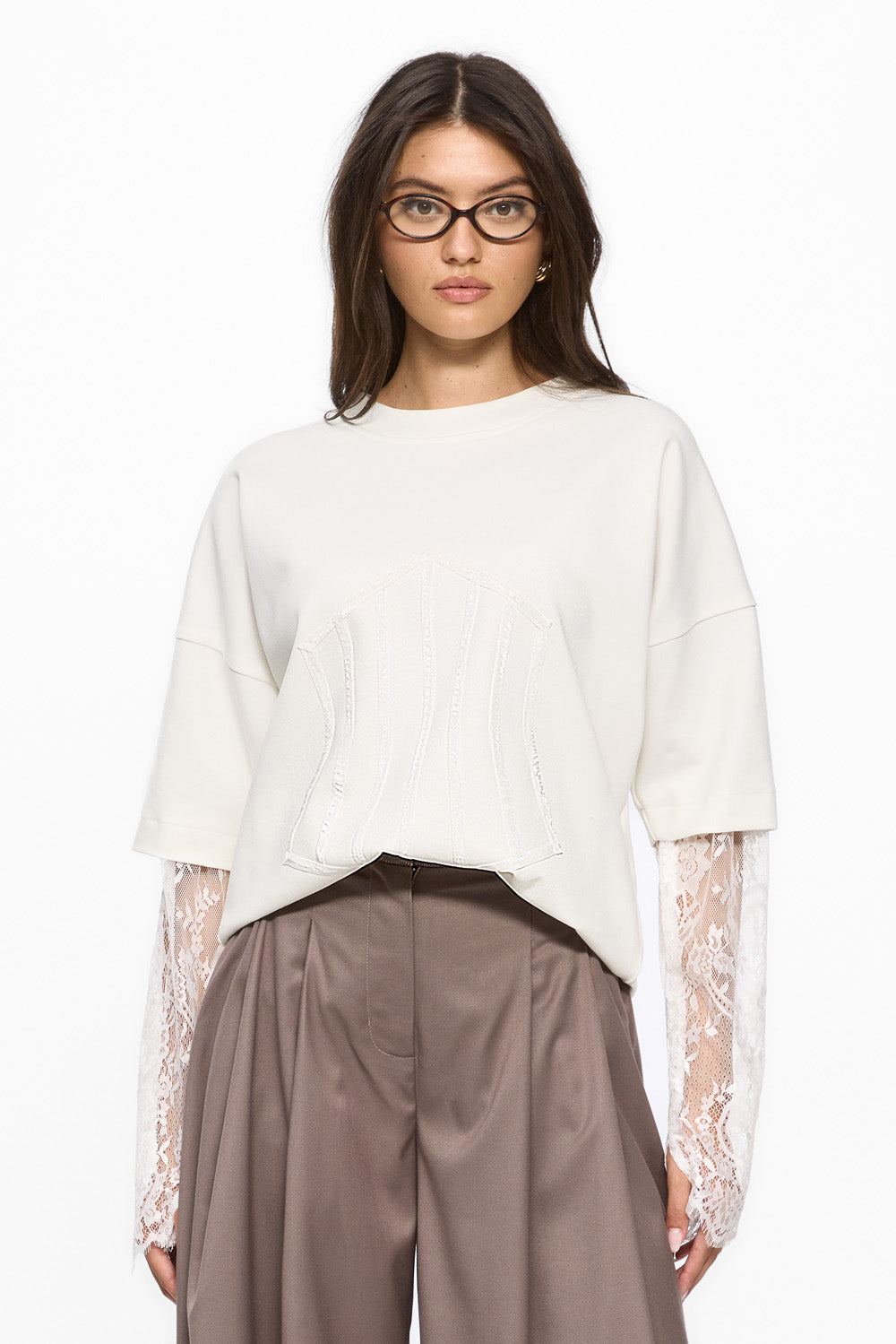Woman wearing a white blouse with lace sleeves and brown pants on a white background