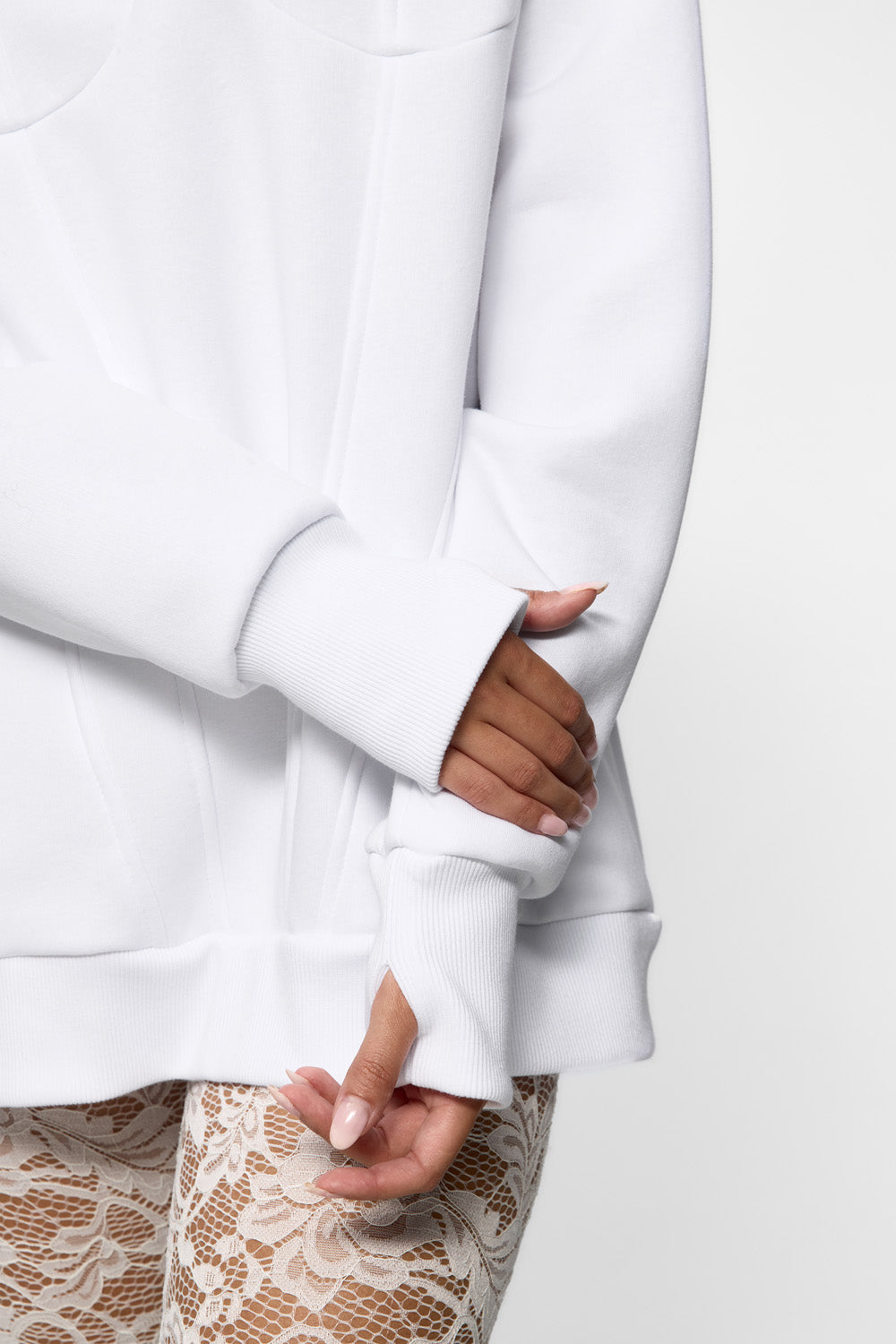 Close-up of a person wearing a white long-sleeve top with lace pants on a light gray background