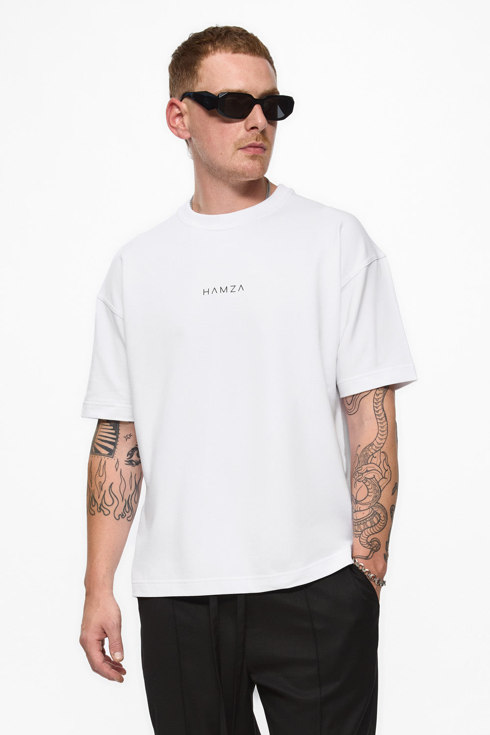 Man wearing a white t-shirt with 'HAMZA' logo and black pants on a white background