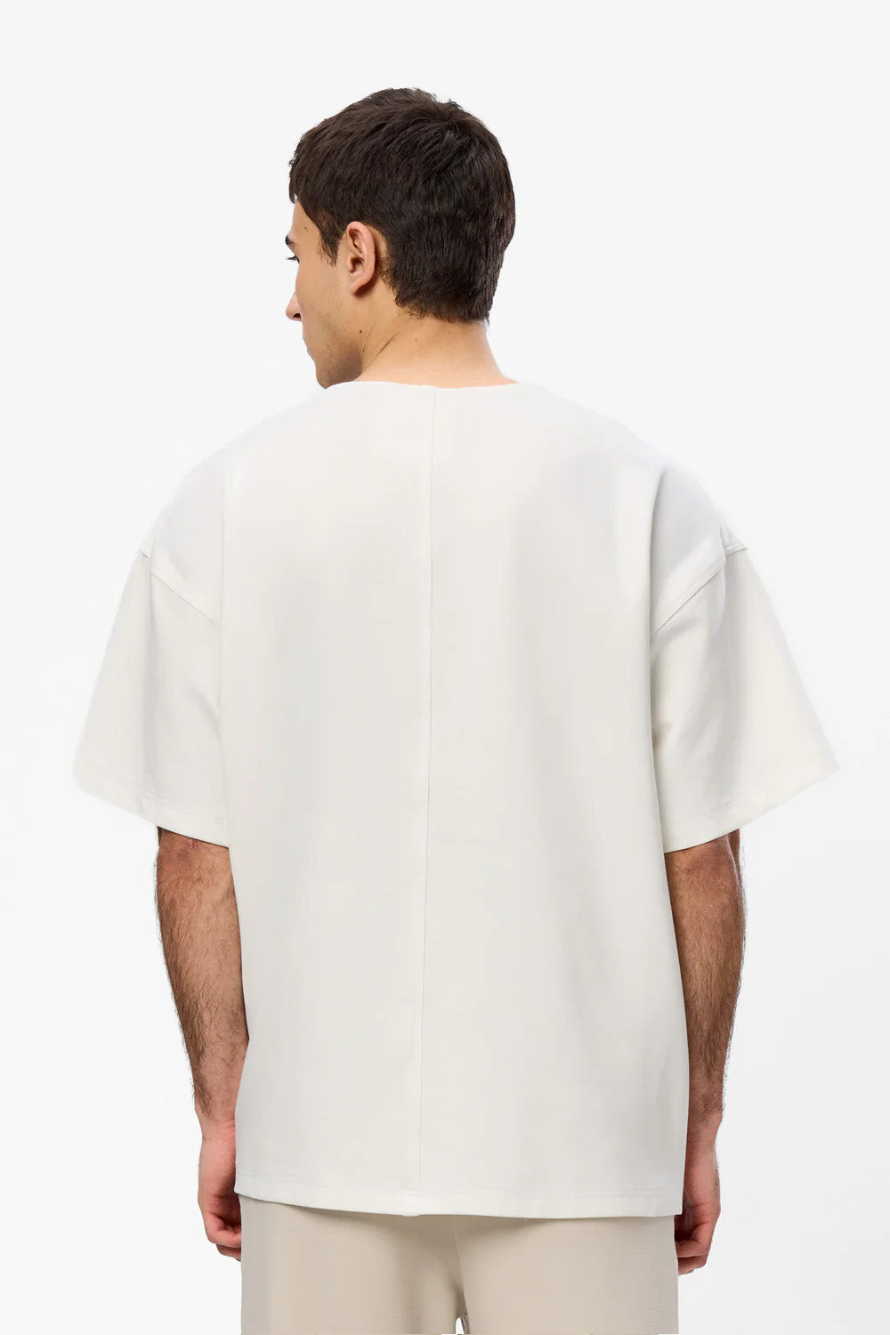 Vedere din spate a unui model purtând tricoul oversized Calm Your Mind Off-White pentru bărbați, evidențiind cusătura decorativă centrală de pe spate